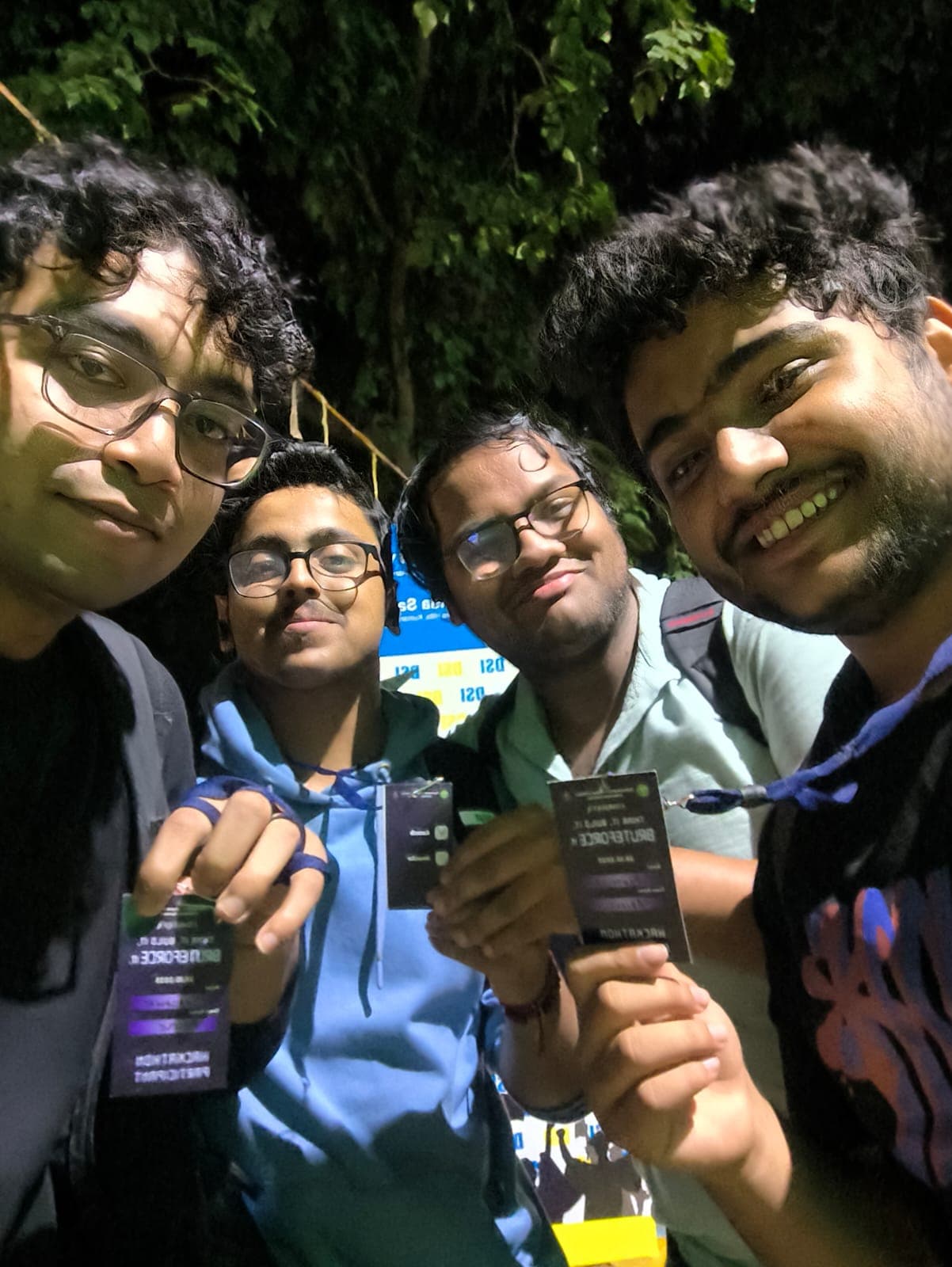 Four teammates leaning into a night selfie, each holding up a Bruteforce hackathon participant badge.